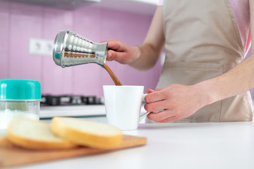 Woman in apron making hot Turkish morning coffee from cezve for breakfast at kitchen close up