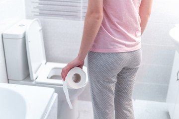 Woman holding a paper roll and suffering from diarrhea, constipation and cystitis at toilet. Stomach pain during PMS. Health care