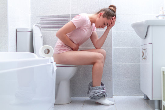 Unhappy woman suffering from diarrhea, constipation and stomach pain at toilet. Treatment abdominal pain and food poisoning. Health care