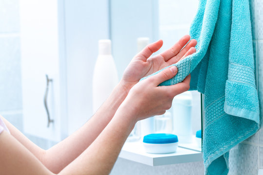 Woman wipe hands dry with towel after washing in bathroom at home. Hygiene and hand care.