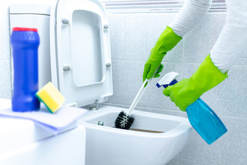 Housewife in rubber gloves cleaning and disinfecting toilet using cleaning products and a brush. Cleaning service