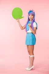 Full length view of asian anime girl holding green speech bubble and showing idea sign on pink