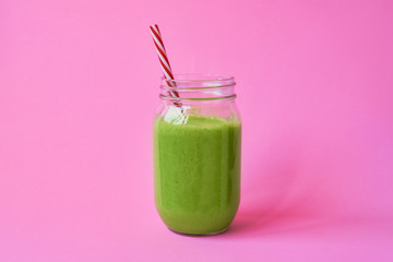 Healthy green smoothie in a jar mug on pink background. Copy space