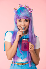 Smiling asian anime girl drinking beverage isolated on pink