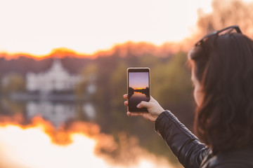 woman taking picture of sunset on her phone - Powered by Adobe