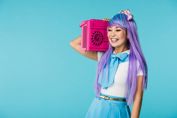 Smiling asian otaku girl in purple wig holding boombox isolated on blue