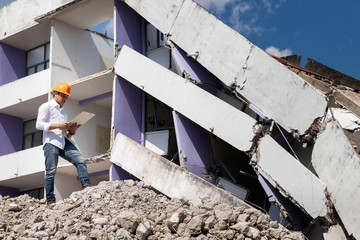 Engineer holding laptop is checking for destruction, demolishing building.