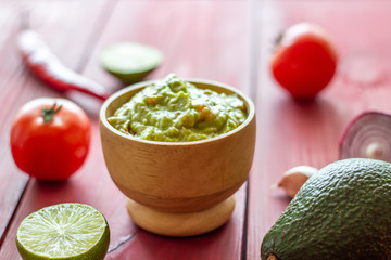 Guacamole and ingredients. Red background. Mexican cuisine.