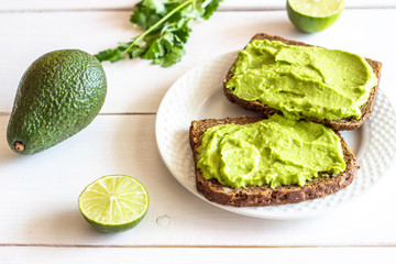 Sandwiches with avocado on the white wooden background.