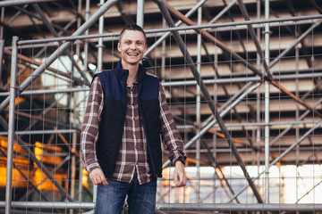 Fototapeta premium Cute young hipster man posing against a background of barred building with iron structures. The concept of tourist walks around the city