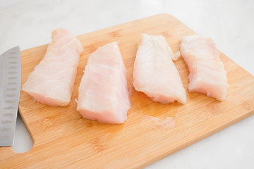 Grouper Fillets on a Cutting Board: Four raw fish fillets on a bamboo chopping board with a santoku knife