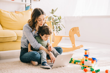 Mom and son sitting on carpet and using laptop