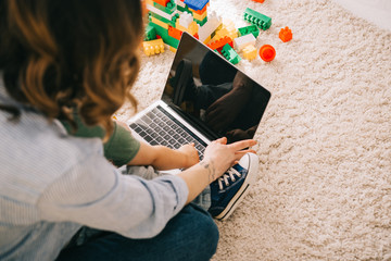 Cropped view of mother and son sitting on carpet and using laptop
