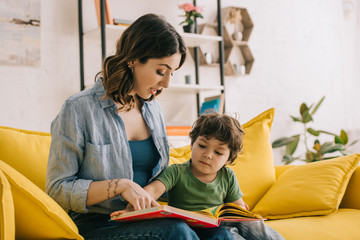 Mom and son sitting on yellow sofa and reading book