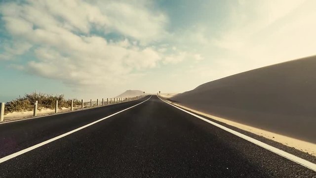 Travel and drive concept - long way road asphalt viewed from car nose ground level moving under and fast - scenic landscape desert sand style around and in background - traveling and enjoying vacation