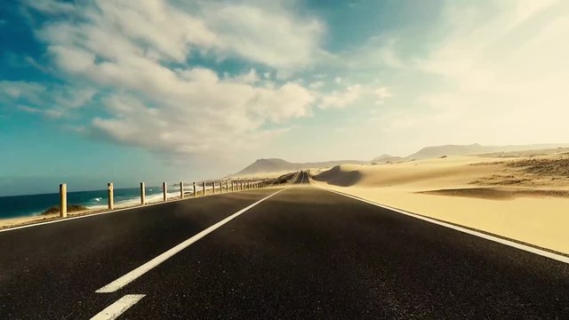 Travel and drive concept - long way road asphalt viewed from car nose ground level moving under and fast - scenic landscape desert sand style around and in background - traveling and enjoying vacation