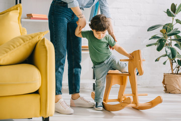 cropped view of mother and son with wooden rocking horse