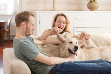 Happy lovers newlyweds enjoying a weekend in the room of their cozy country house sitting on the sofa with their beloved dog