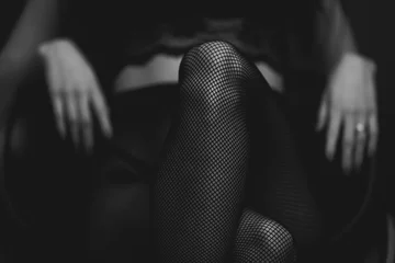 slim sexy woman in black stockings sits on a chair on a black background. black and white © Rychko Yevhen