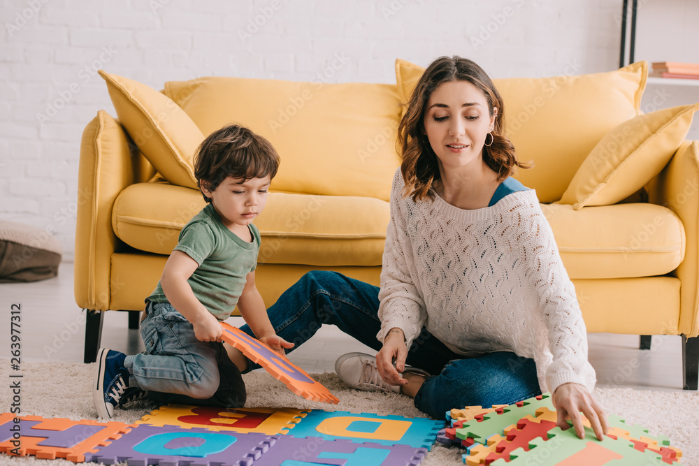 Wall mural Mother and son playing with alphabet puzzle mat on carpet