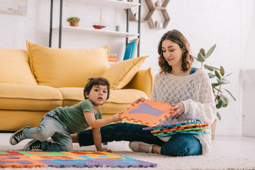 Obraz premium Smiling mother and kid playing with alphabet puzzle mat