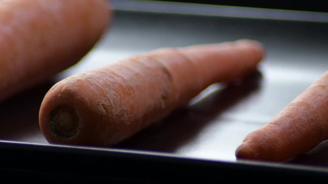 Carrots gyrating on a black tray with black background. Daucus carota