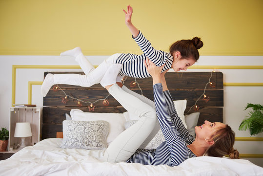Mother and daughter playing on bed, pretending to fly