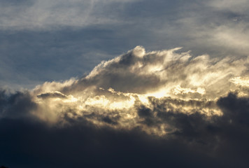 The sun behind dense cumulus clouds lights up their edge at the afternoon above the Andean mountains of central Colombia.