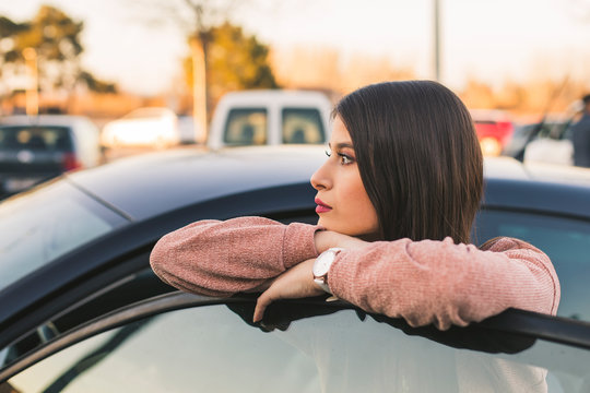 Teenage girl leaning on car door looking at distance