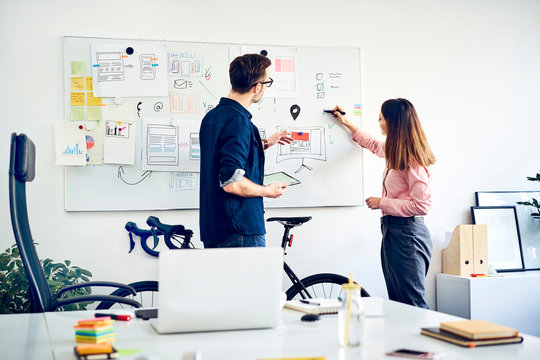 Two colleagues discussing at whiteboard in office