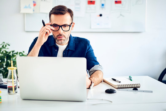 Casual businessman working on laptop at desk in office
