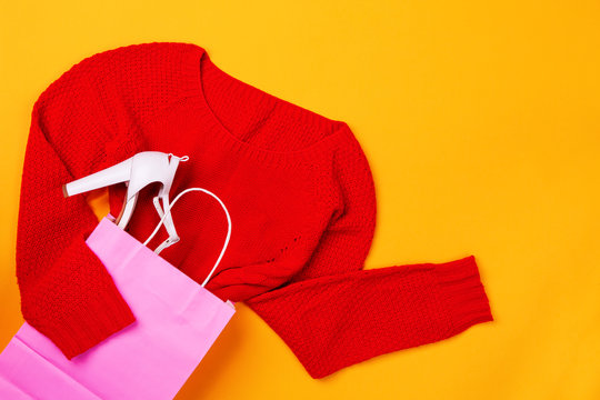 Top view of pink shopping bag with red swether and stylish shoes