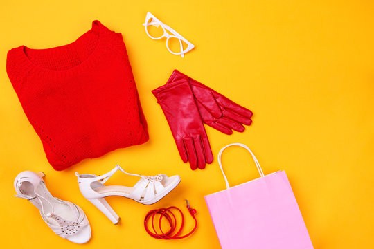 Top view of red swether, red belt and gloves, white stylish shoes and glasses and pink shopping bag
