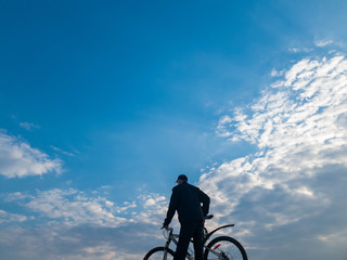 Fototapeta premium Man with a bicycle against the sky. Cyclist on the top.