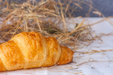 Crispy fresh croissant closeup on a white towel on background of hay and gray walls.