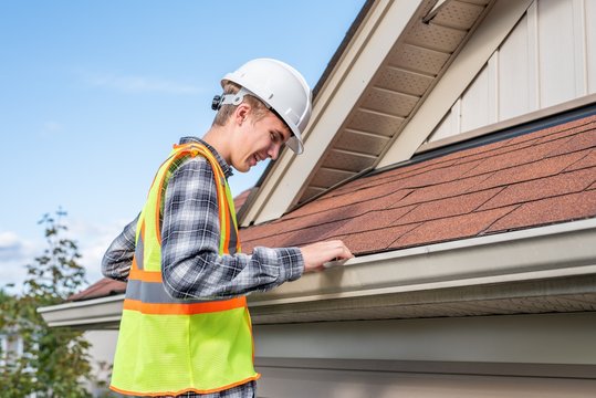 Home Inspector Standing On A Ladder And Providing An Inspection To The Roof Of A House.