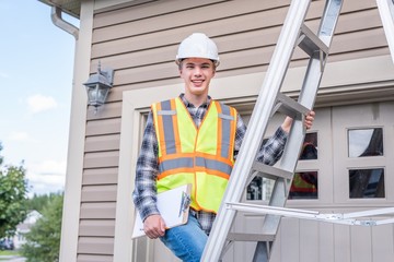 Young male architect standing on a ladder and dressed in safety gear.