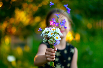 Fototapeta na wymiar Little cute girl with bouquet of wildflowers. Сhild gives flowers to mom. Close uo view on the hand with present.