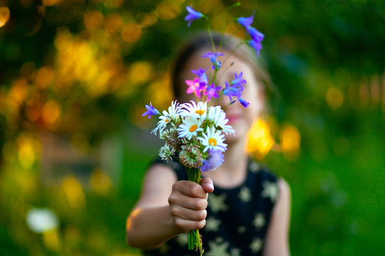 Little cute girl with bouquet of wildflowers. Сhild gives flowers to mom. Close uo view on the hand with present.