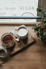 High angle view of tiramisu in glass cup with coffee cappuccino. In vegsn shop, local cozy cafe. Wooden background, candid style. Copy space