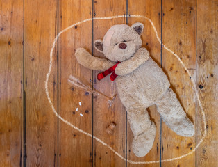 Teddy bear lying on floor with an empty glass, pills and chalk outline. Concept.