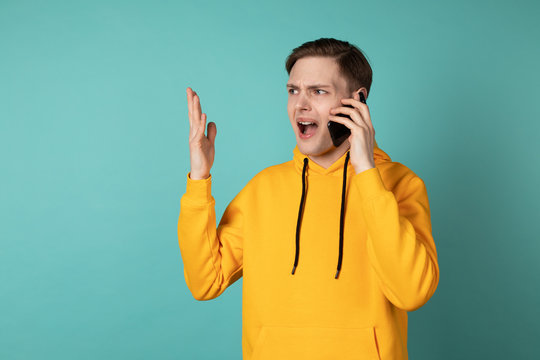 Image of young screaming man in yellowe hoodie standing isolated over blue wall background - Powered by Adobe