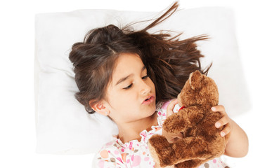  Little girl in bed with teddy bear the emotions of a child, white bed. Isolated on white background