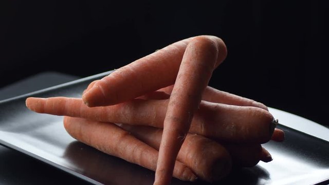 Raw carrots vegetables gyrating on a black tray. Daucus carota
