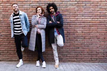 Portrait of three friends standing at a brick wall