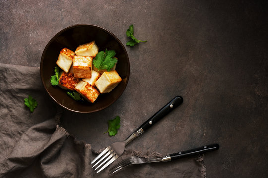 Fried tofu cheese in a bowl with greens on a dark background. Top view, copy space.