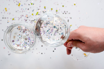 The clink of glasses. Glasses with sparkles inside. Glitter elements in drink. Happy party event. Celebrate the holiday. Alcohol drink - wine, champagne. Magic festive moment. Glass in hand. Cheers!