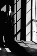 Fototapeta na wymiar black and white portrait of a stylish businessman near the window and the shadow of which leaves a mark on the face of a man
