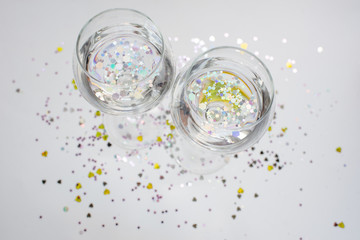 The clink of glasses. Glasses with sparkles inside. Glitter elements in drink. Happy party event. Celebrate the holiday. Alcohol drink - wine, champagne. Magic festive moment. Glass in hand. Cheers!