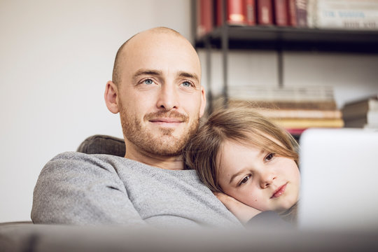 Father and daughter sitting on couch, using laptop
